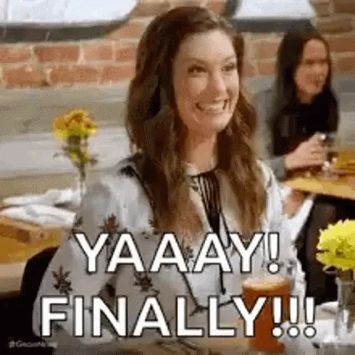 A woman at a restaurant table cheering, captioned “yaaay! finally!!!”