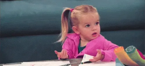 A toddler at a desk, palms up, shrugging