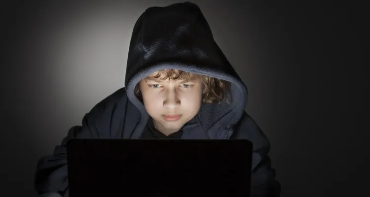 A child in a hoodie lit only by a laptop screen